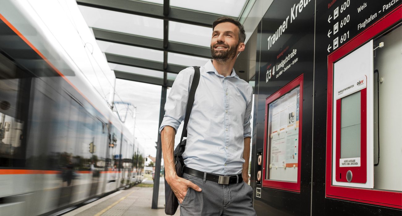 Mann steht an einer Straßenbahnhaltestelle und die Straßenbahn fährt gerade ein.